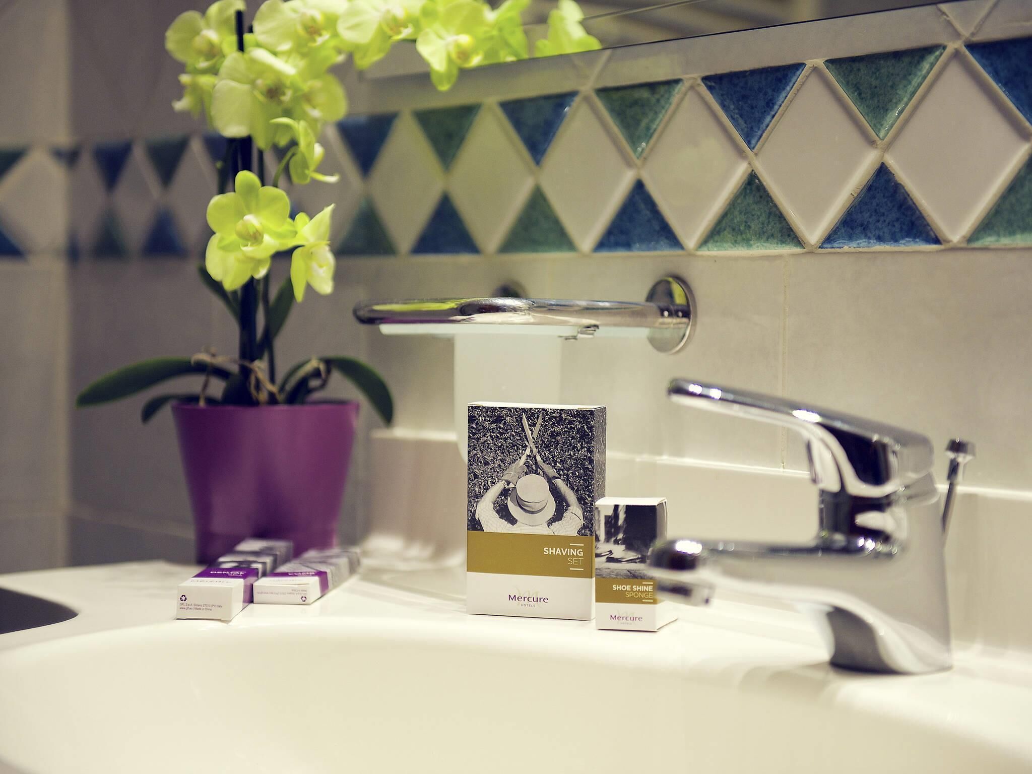A bathroom with a sink, a potted orchid, and a shaving set on the counter.
