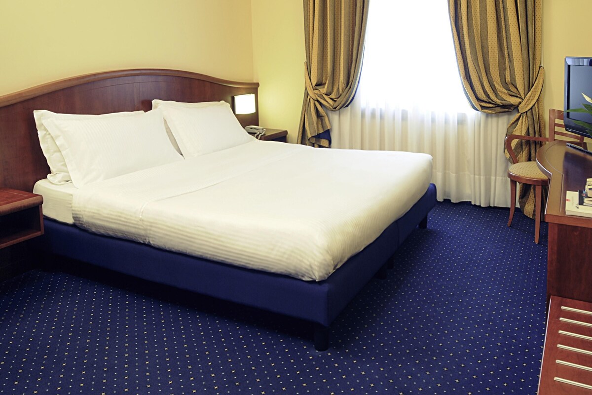 A hotel room with a large bed, a desk, a chair, and a TV.