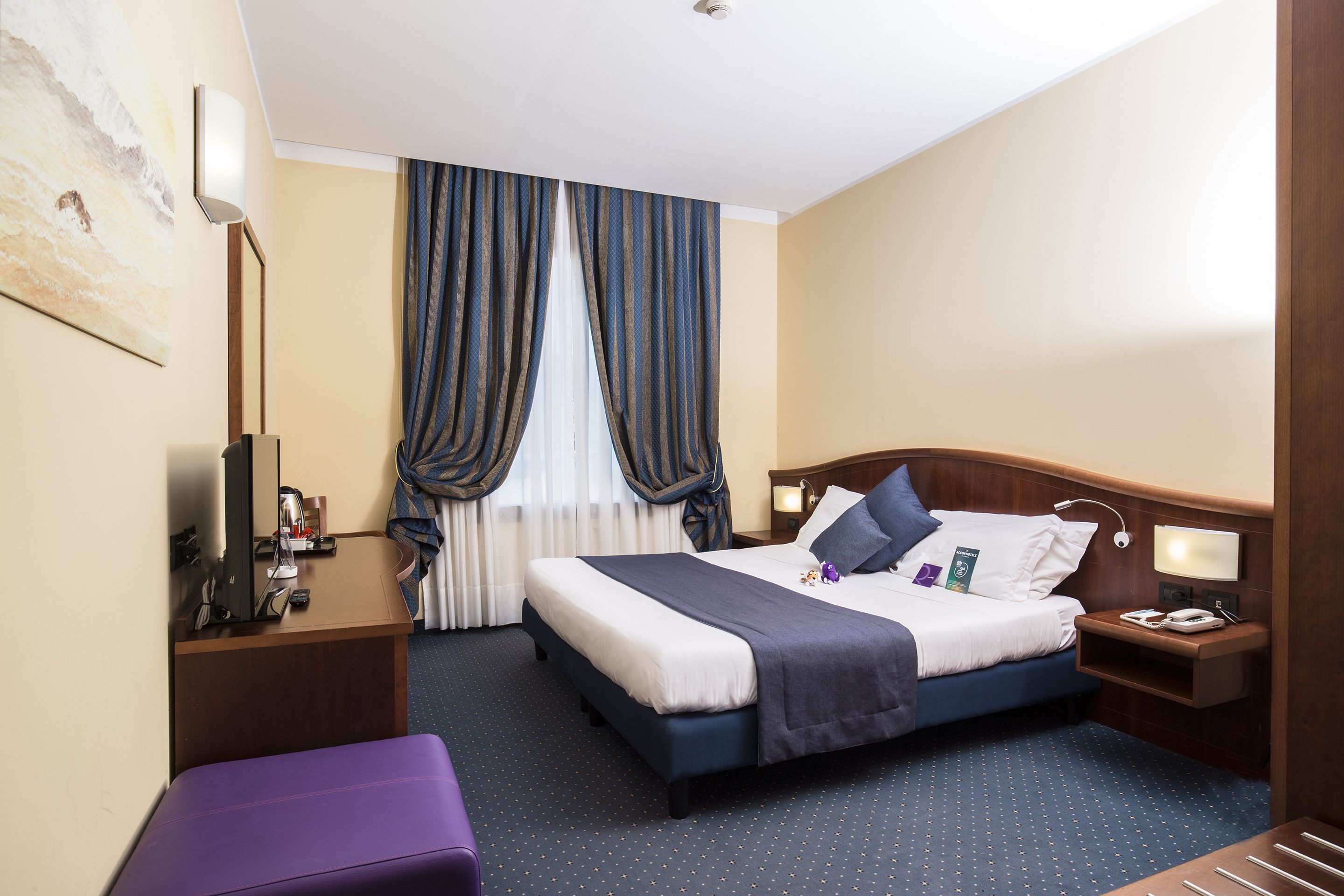 Ein Hotelzimmer mit Bett, Nachttischen, Schreibtisch, Stuhl und einem Fenster mit Vorhängen.