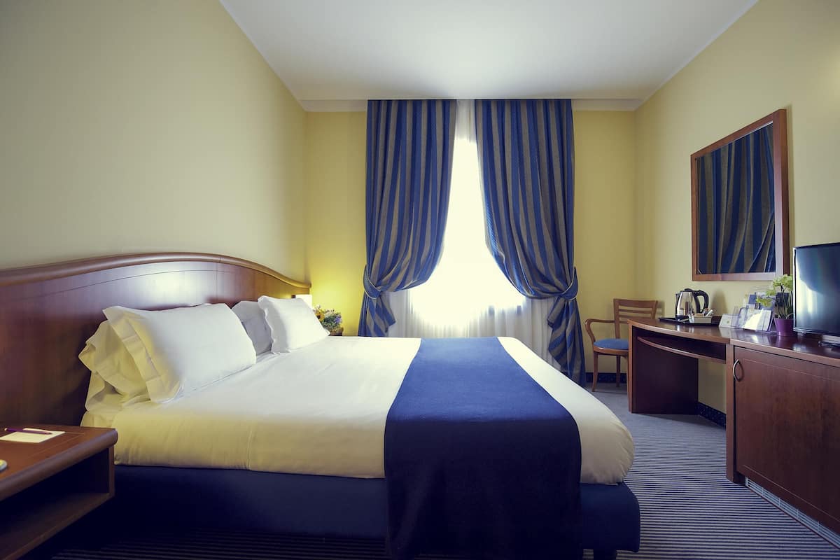 A hotel room with a bed, a desk, a chair, a television, and curtains.