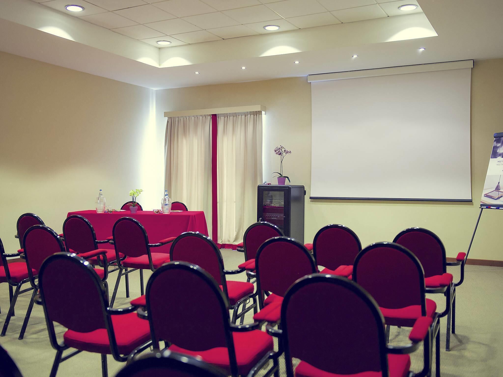 Un salón de conferencias con una mesa, sillas, una pantalla de proyector y un atril.