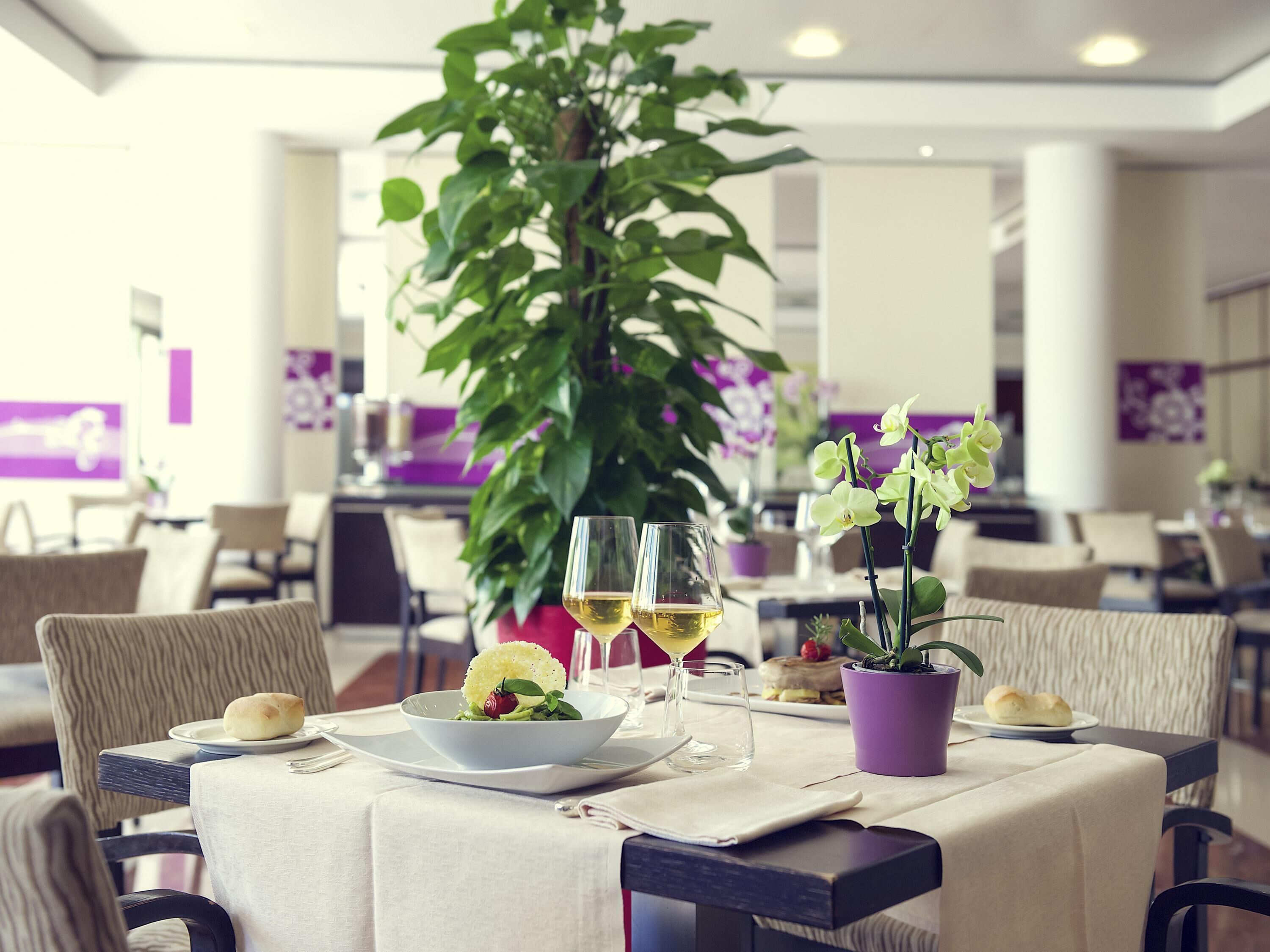 Un comedor con una mesa dispuesta para dos personas, que incluye un tazón de ensalada, dos copas de vino y una planta en maceta.