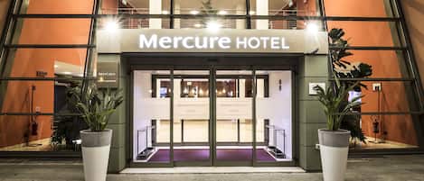 The entrance to Mercure Hotel with a modern design, featuring large glass doors and potted plants.