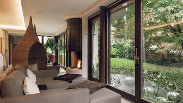 A modern living room with a sofa, a fireplace, and a view of a garden.