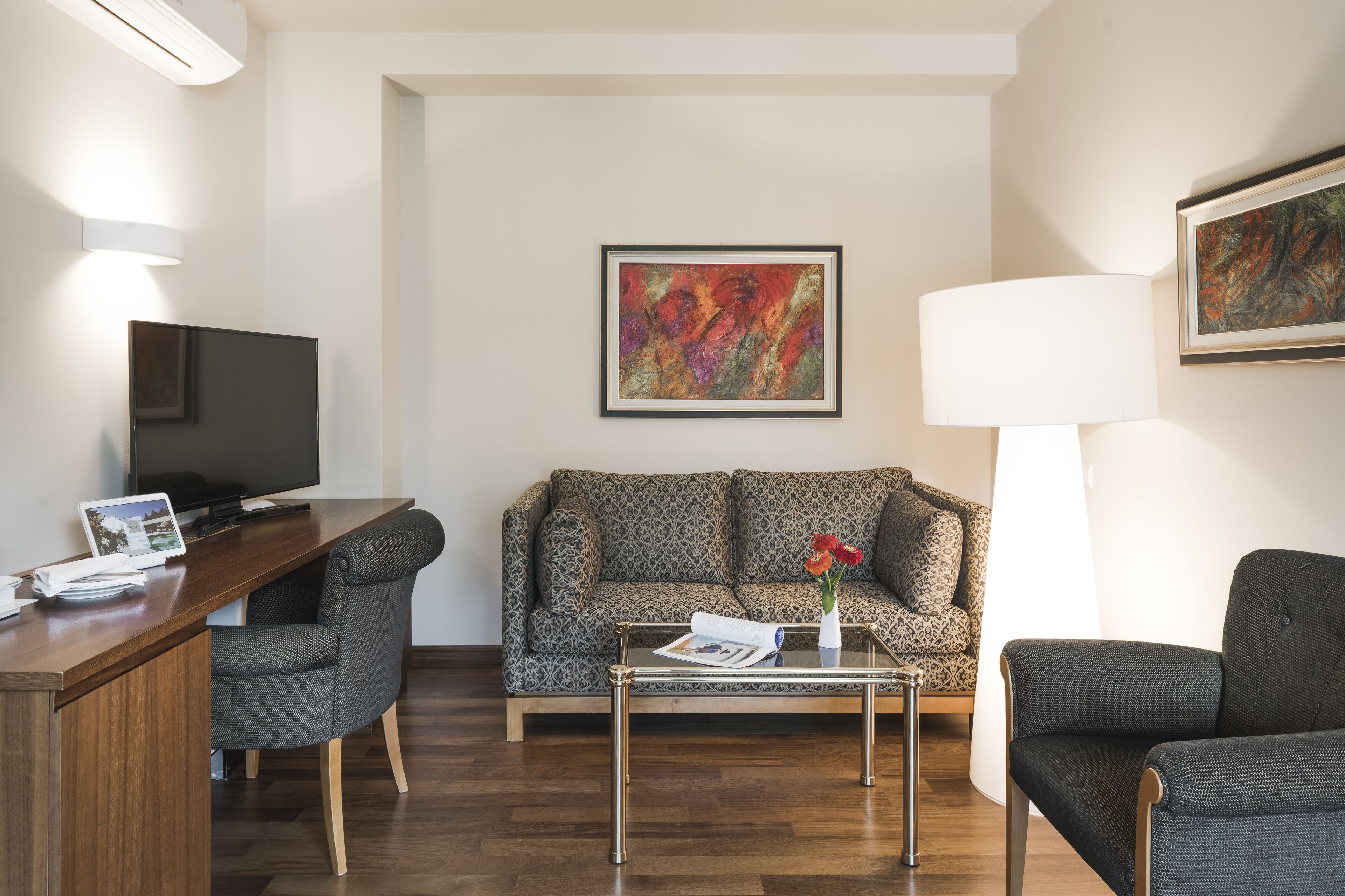 Ein modernes Wohnzimmer mit einer Couch, zwei Sesseln, einem Couchtisch, einem Fernseher und einem Gemälde an der Wand.