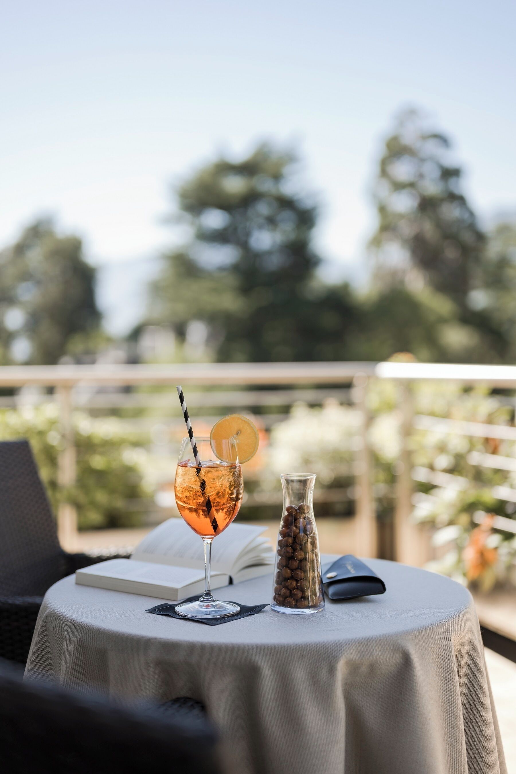 A round table with a drink, a book, and a small vase on a balcony.