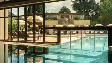 Ein Schwimmbecken mit klarem Wasser, umgeben von Liegestühlen und Sonnenschirmen, mit Blick auf Bäume und ein Gebäude im Hintergrund.
