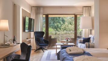 Habitación de hotel con cama, escritorio, silla, televisión y balcón con vistas a árboles.