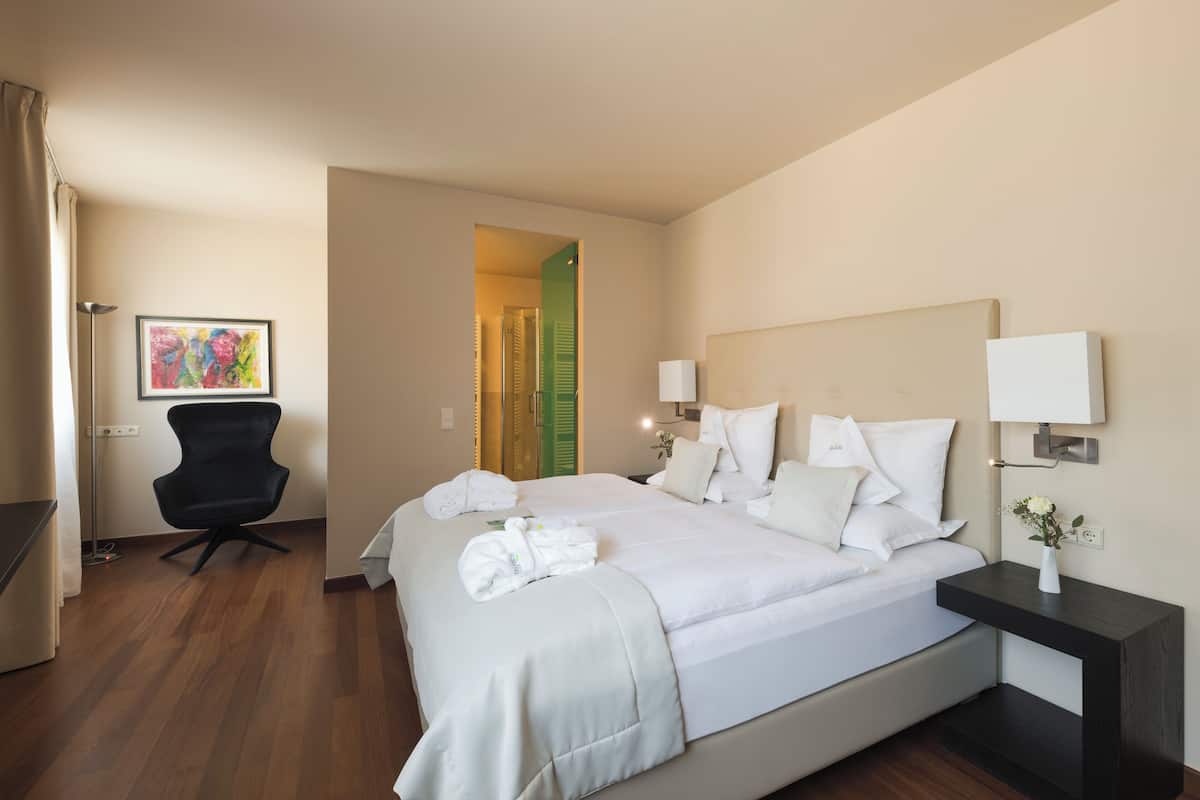 Una habitación de hotel con una cama grande, una silla, un escritorio y un cuadro en la pared.