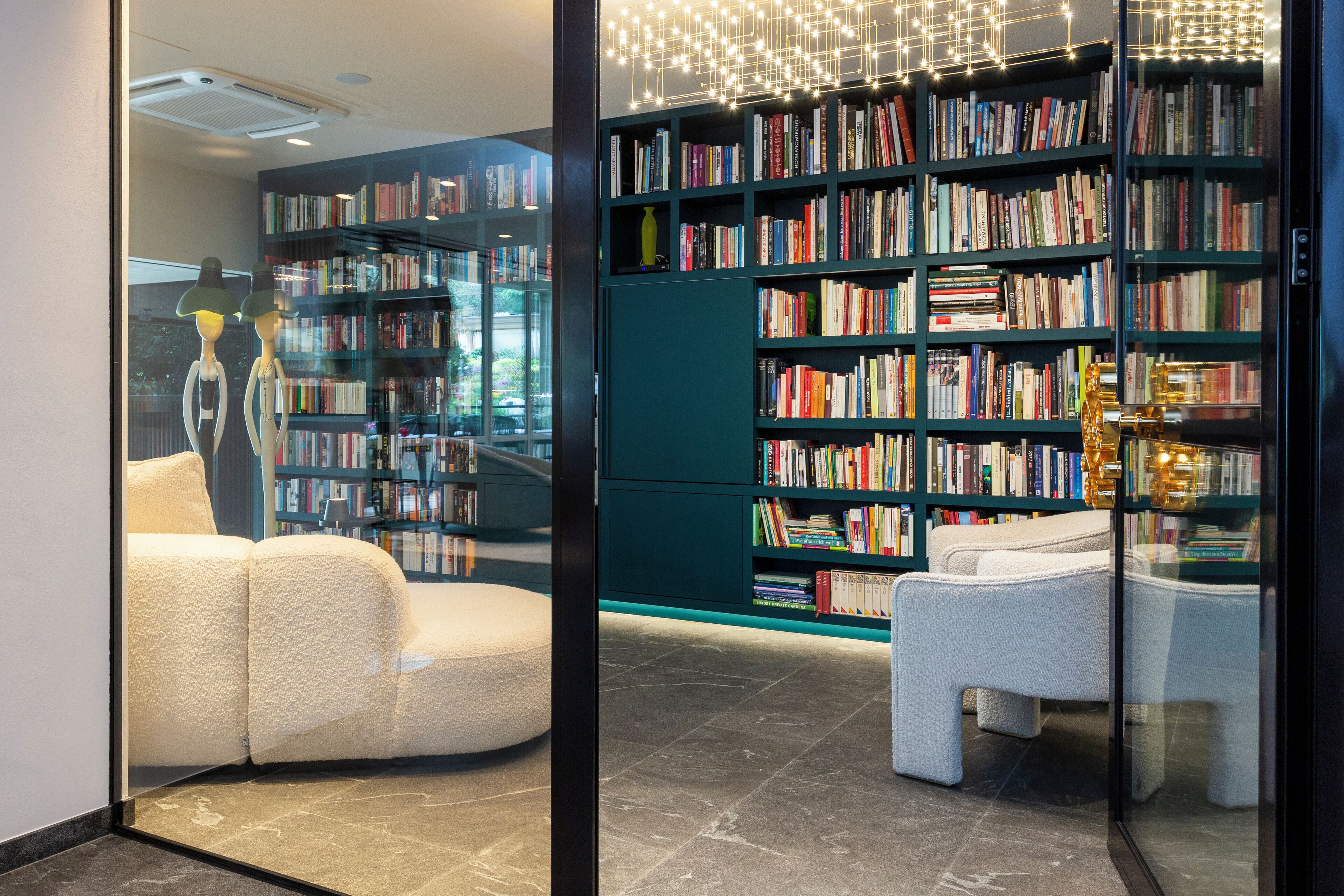 A modern library with bookshelves, comfortable seating, and a glass partition.