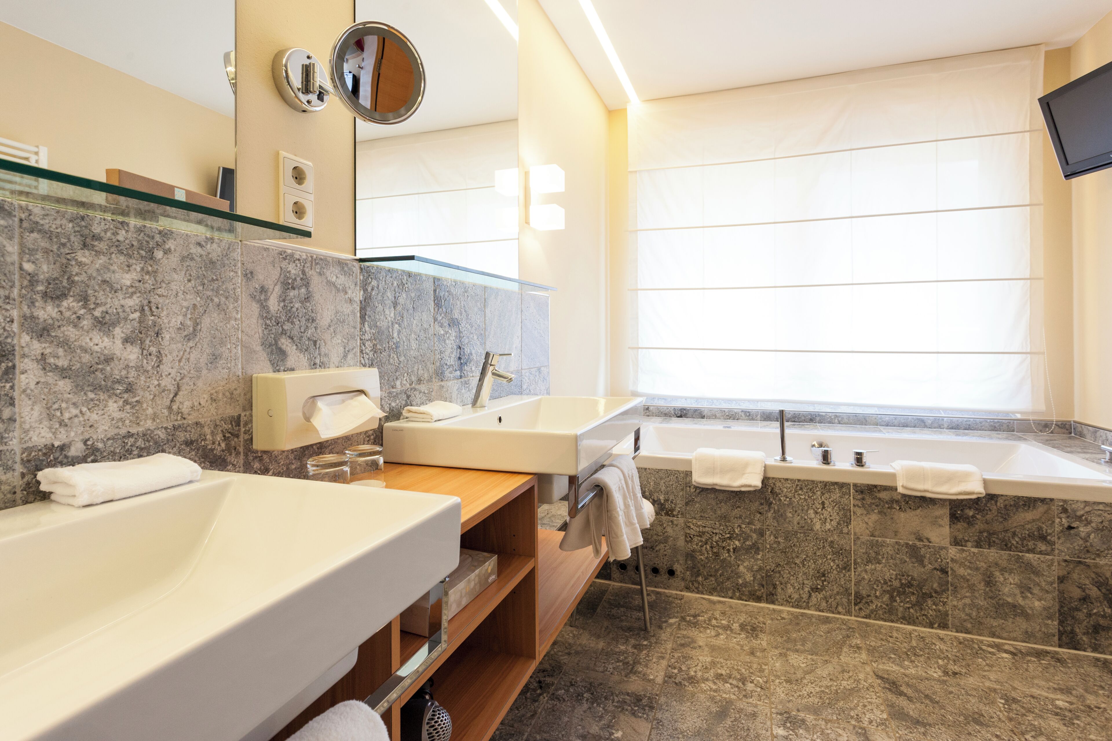 Ein modernes Badezimmer mit einer großen Badewanne, zwei Waschbecken, einem Waschtisch und einem großen Spiegel.