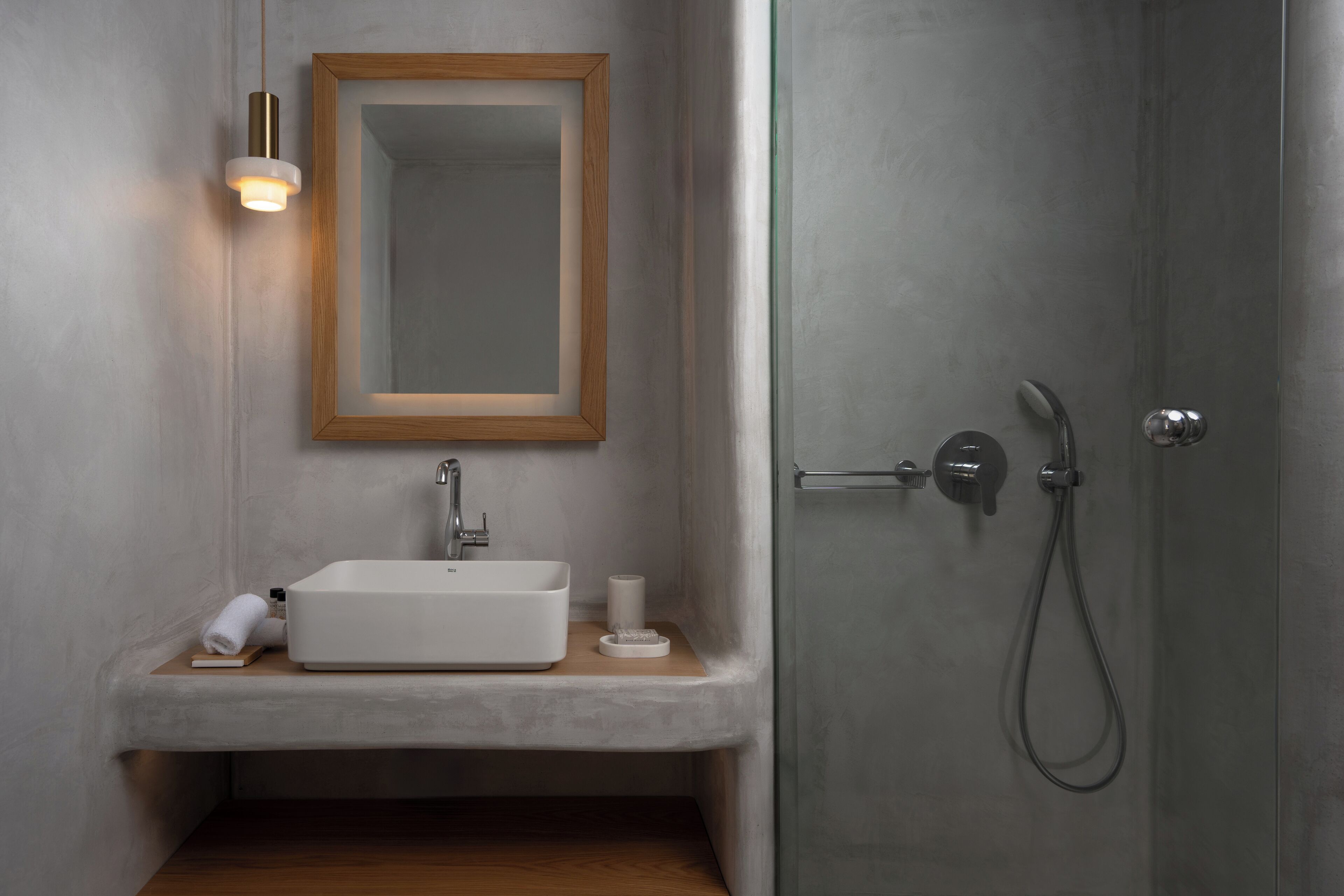 Un baño moderno con un lavabo blanco, un espejo con marco de madera y una ducha con cabezal de ducha manual.