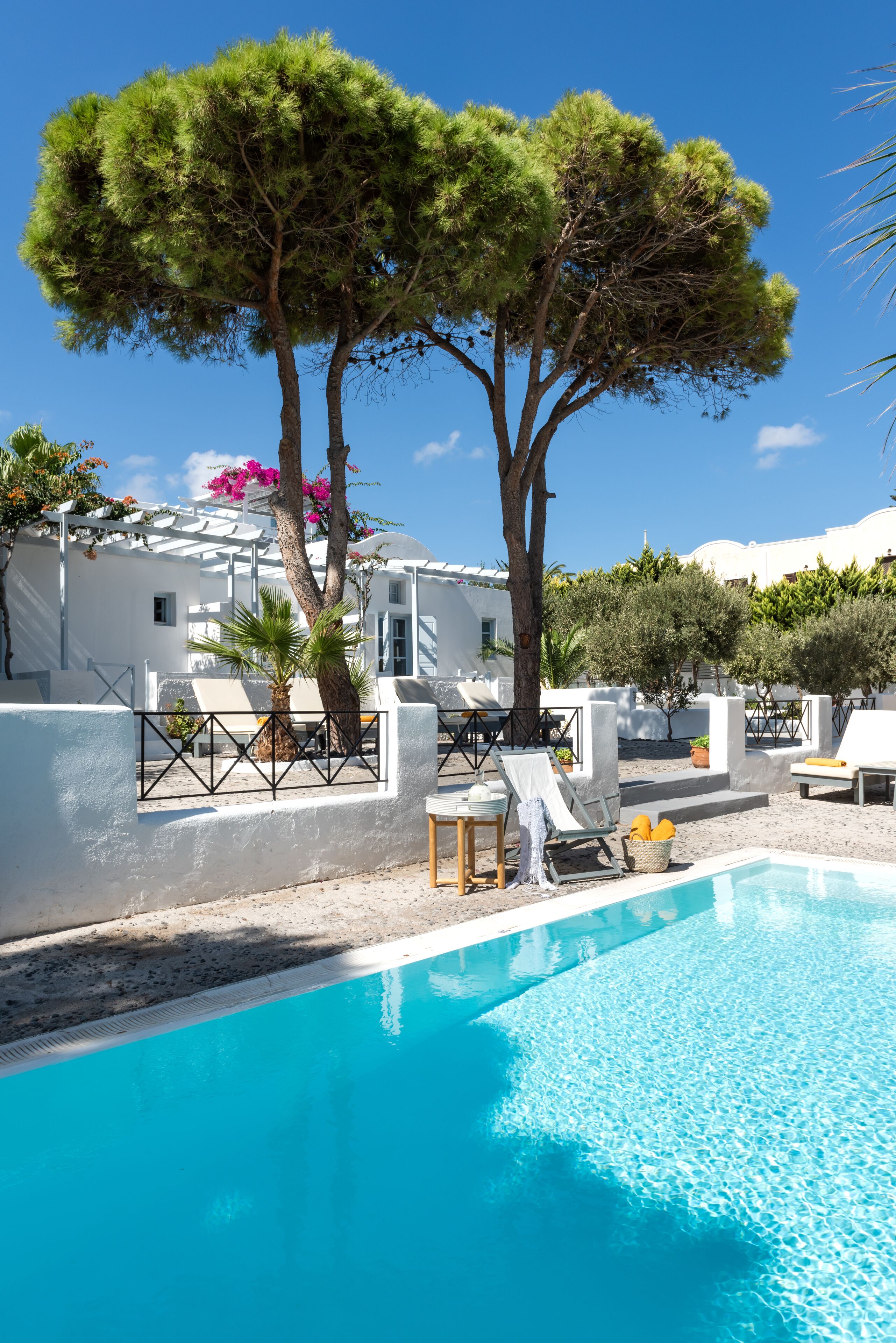 Un espace piscine avec des chaises longues, un bâtiment blanc et des arbres.