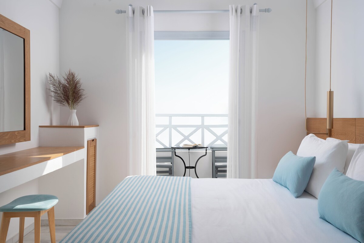 Habitación de hotel con cama, escritorio, silla y balcón con mesa y sillas.