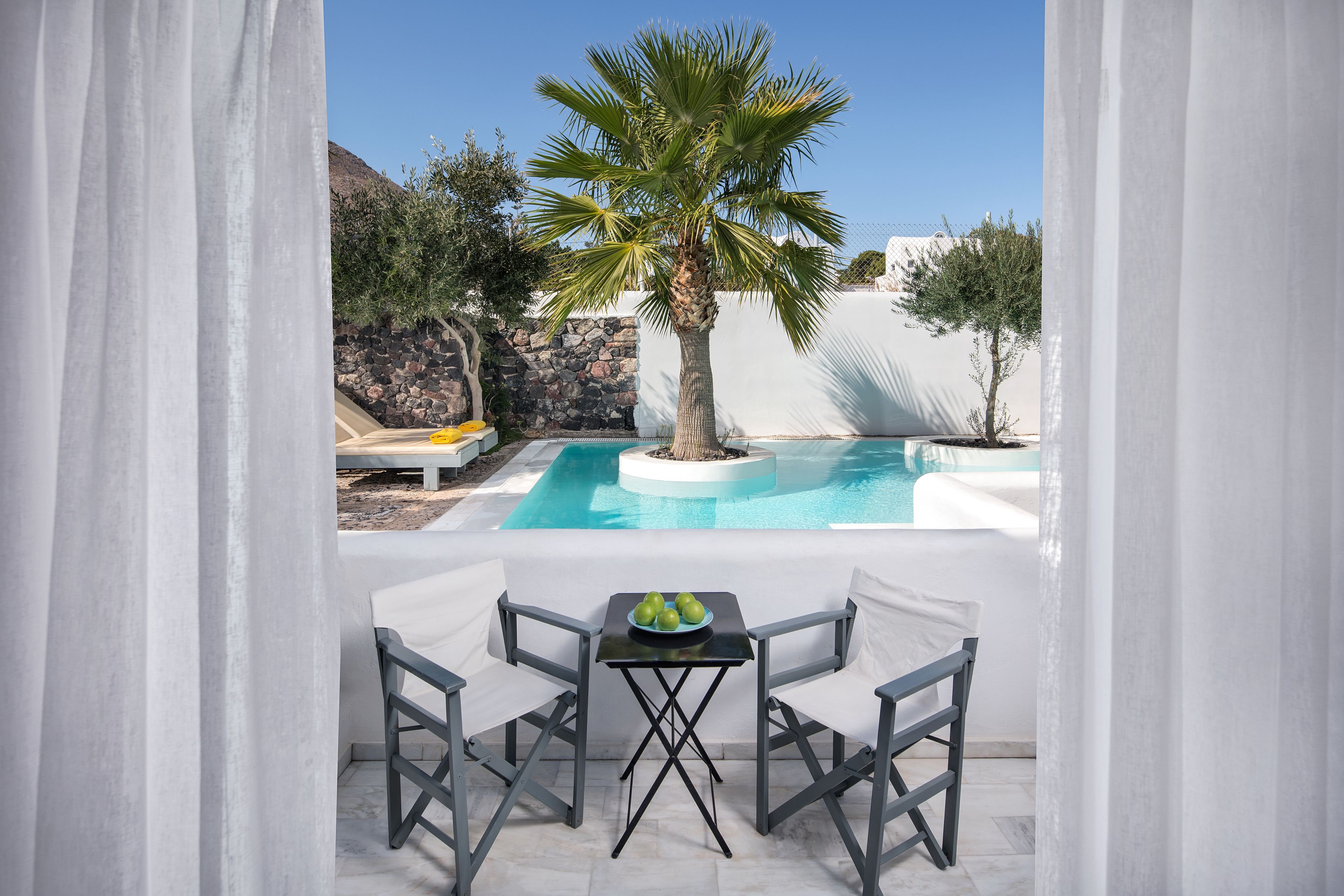 Ein Poolbereich mit Tisch und Stühlen, einer Palme und einer Steinmauer.