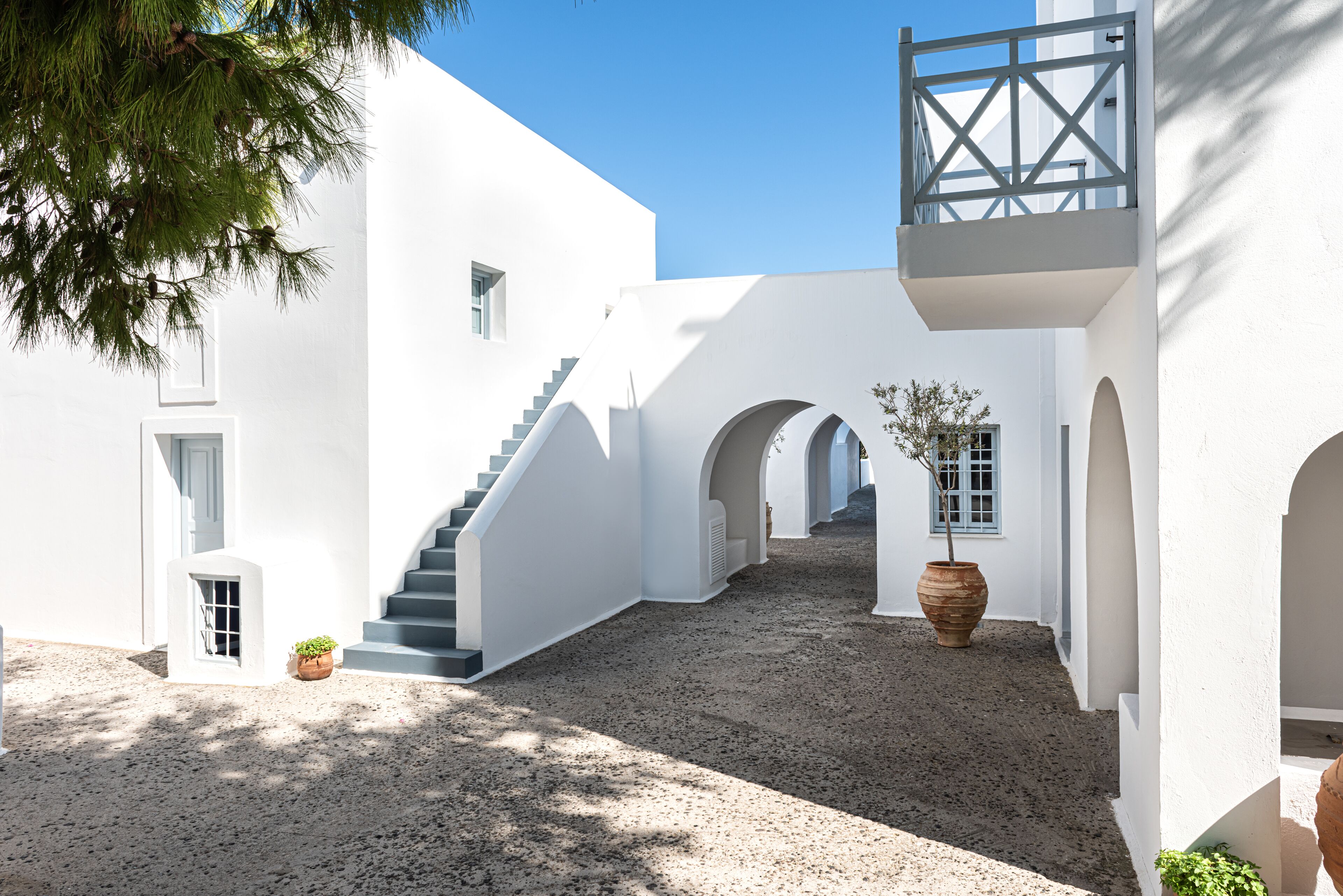 Un edificio blanco con escaleras, pasillos en arco y plantas en macetas.