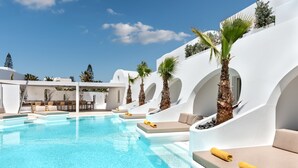 A pool area with white walls, palm trees, and lounge chairs. - Santorini Kastelli Resort (Santorini)