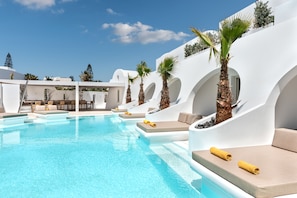 Un espace piscine avec des murs blancs, des palmiers et des chaises longues.