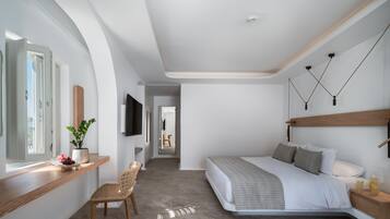 A modern bedroom with a curved bed, a wooden bedside table, a chair, a TV mounted on the wall, and a window with a view of the outdoors.