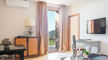 Habitación de hotel con balcón, televisor, escritorio con lámpara y zona de comedor.