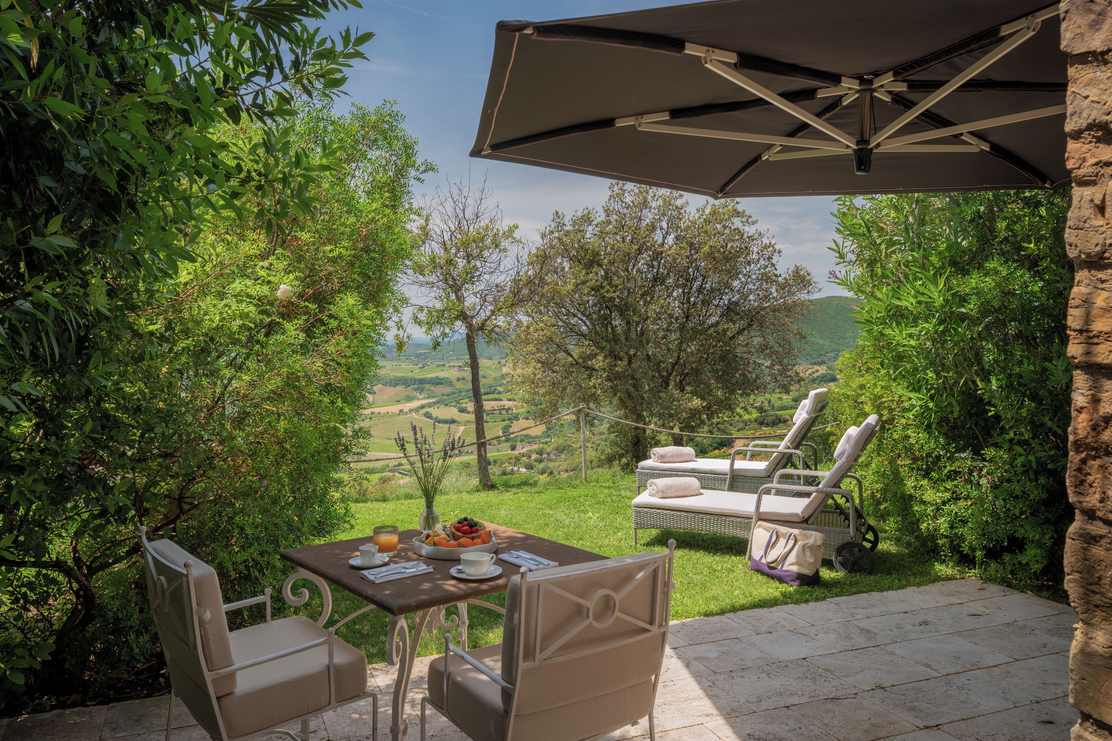 A patio with a table set for two, a lounge chair, and an umbrella.