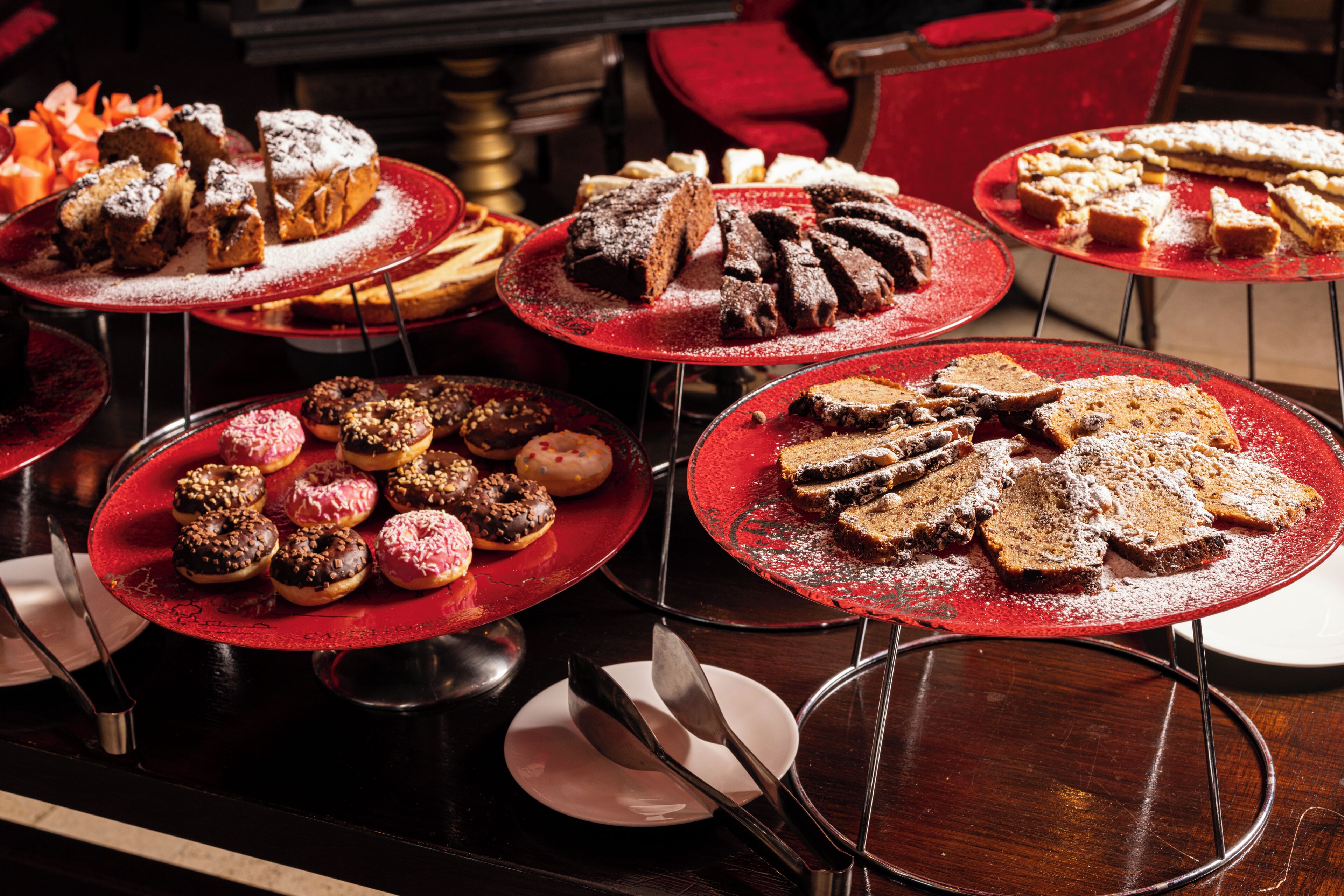 Verschiedene Desserts auf roten Tellern, darunter Kuchen, Brownies und Donuts.