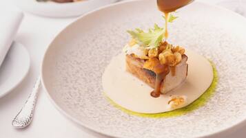 A dessert with a sauce being poured over it, placed on a speckled plate.