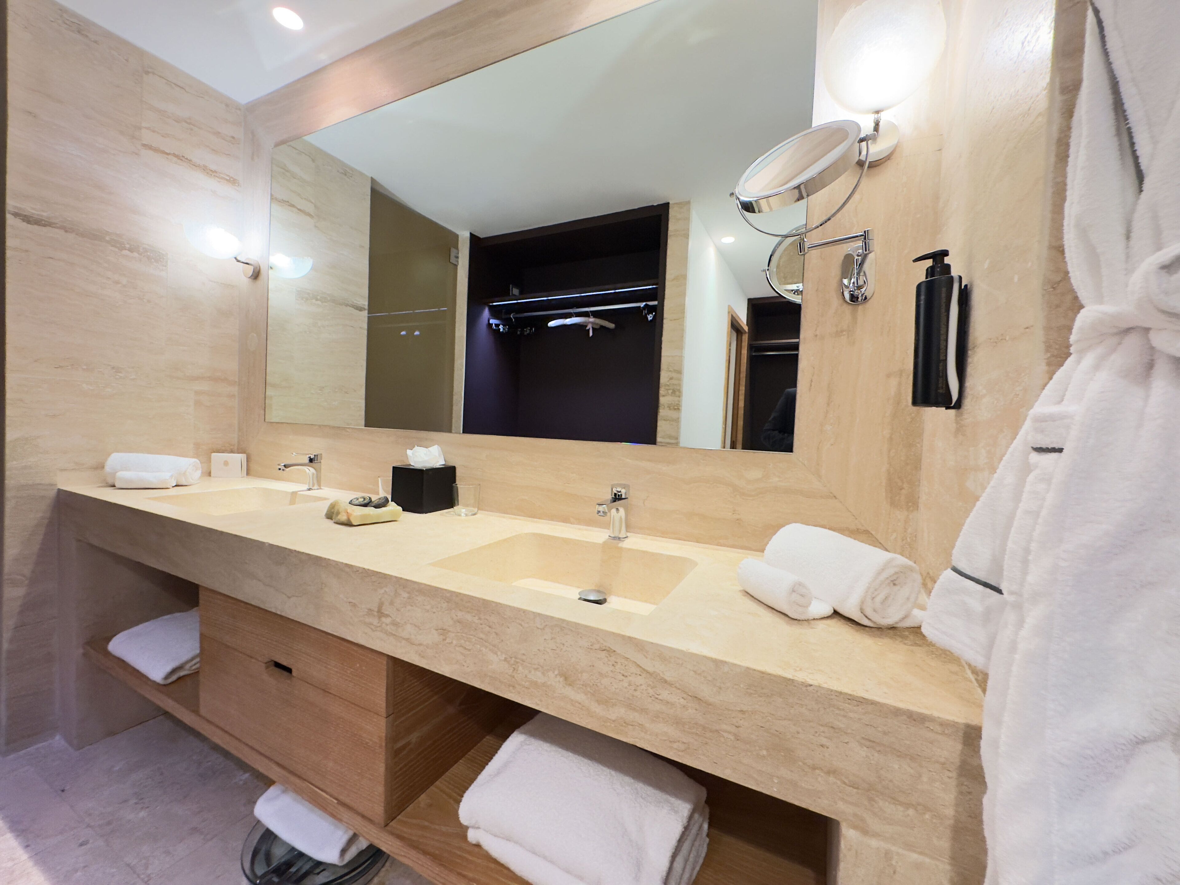 Un bagno moderno con due lavabi, uno specchio grande e un accappatoio appeso a destra.