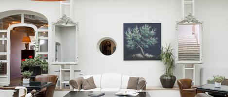 A modern living room with a white sofa, leather armchairs, a glass coffee table, and a large abstract painting.
