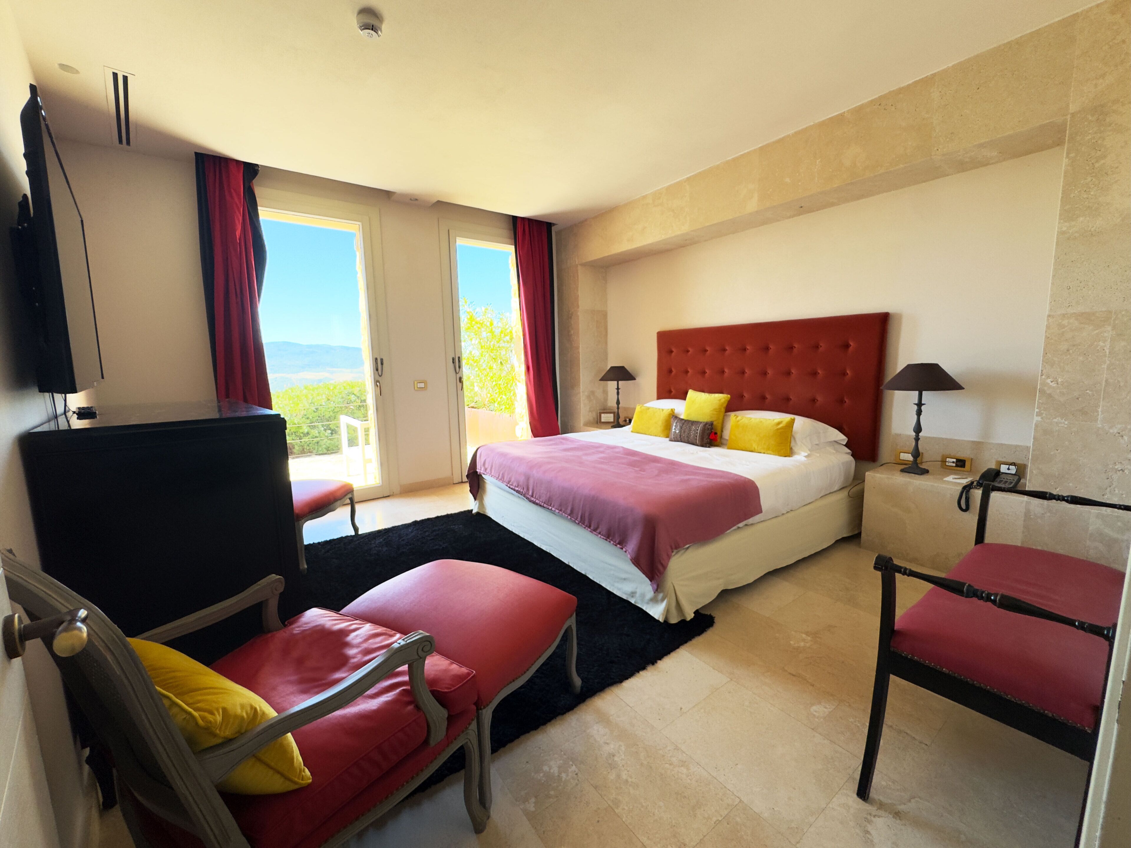 Een hotelkamer met een bed, twee stoelen, een bureau, een televisie en uitzicht op de omgeving.