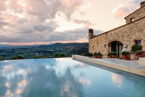 Um edifício de pedra com piscina e vista para uma paisagem montanhosa.