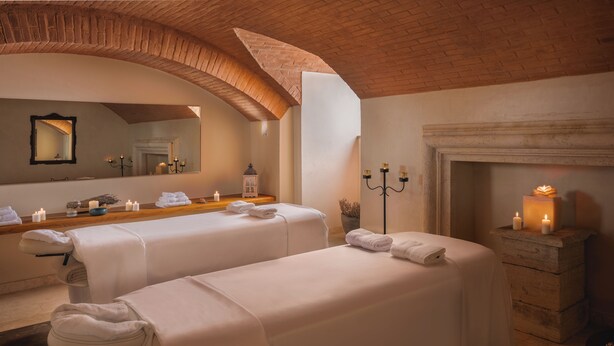 A spa room with two massage tables, a mirror, candles, and a fireplace.