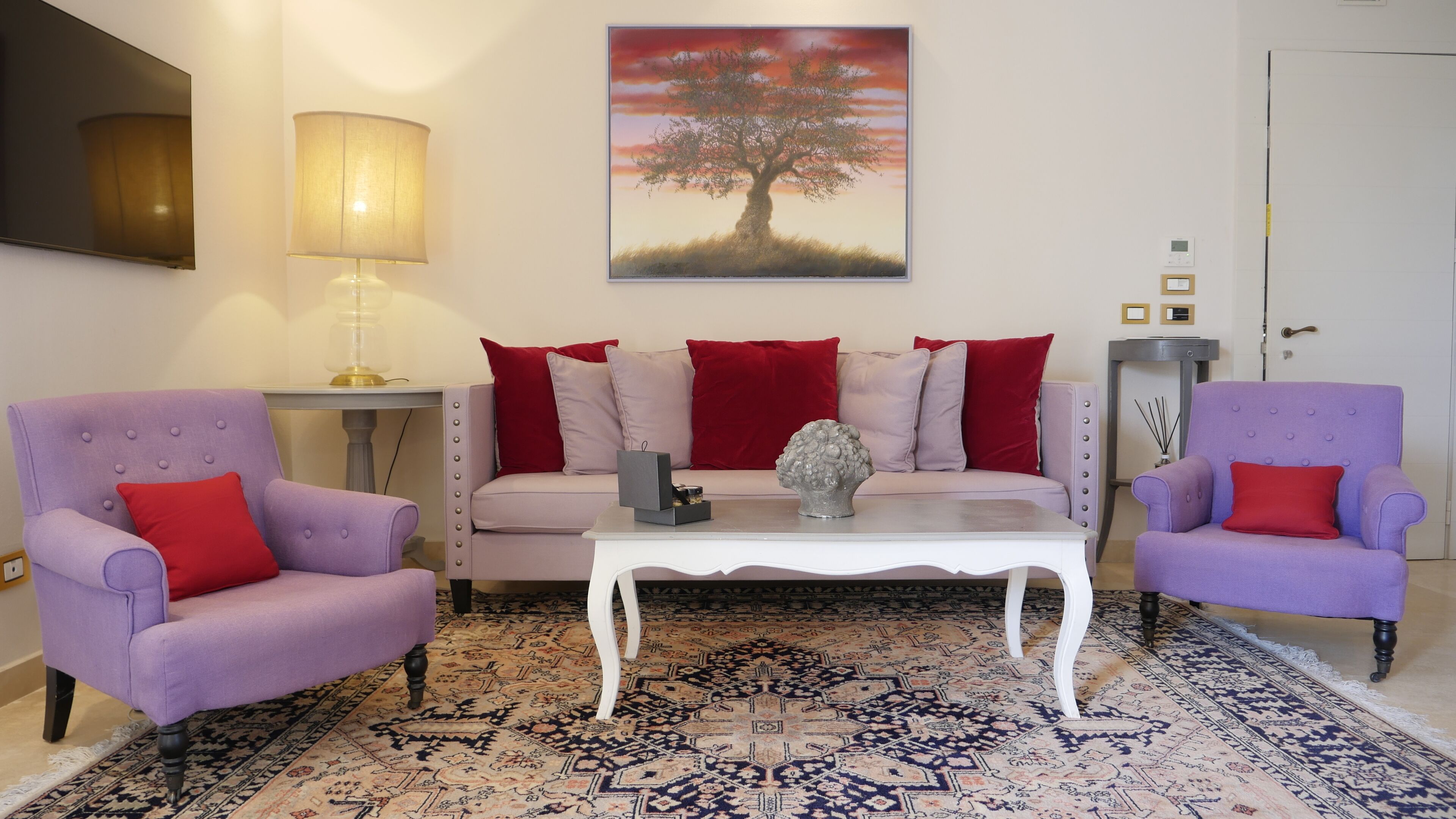 A living room with a sofa set, two armchairs, a coffee table, a lamp, a painting, and a patterned rug.