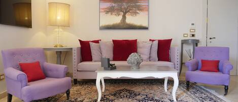 A living room with a sofa set, two armchairs, a coffee table, a lamp, a painting, and a patterned rug.