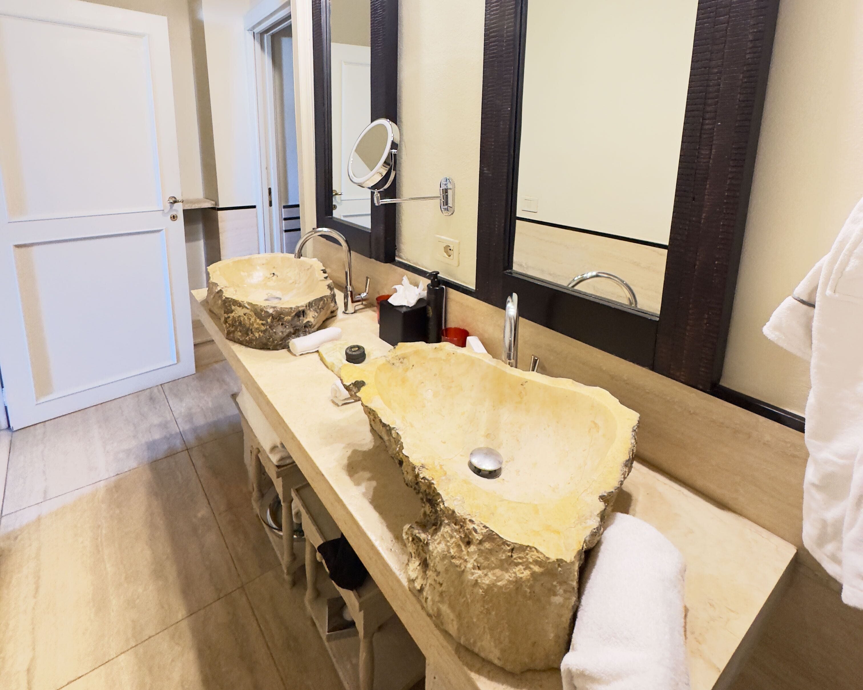 Un baño con dos lavamanos de piedra grandes, un espejo y un perchero para toallas.