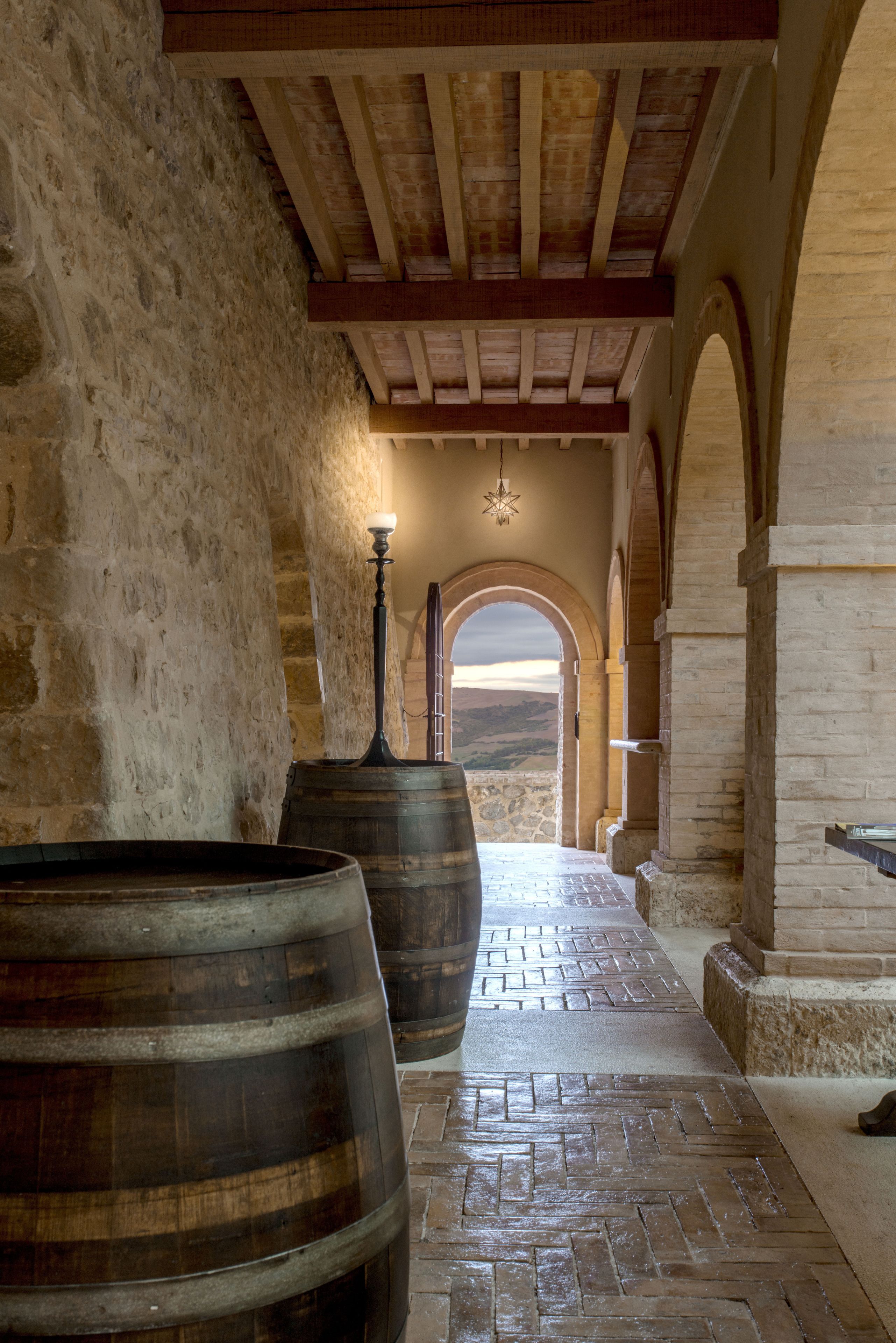 A stone corridor with wooden barrels, arched doorways, and a hanging light fixture.