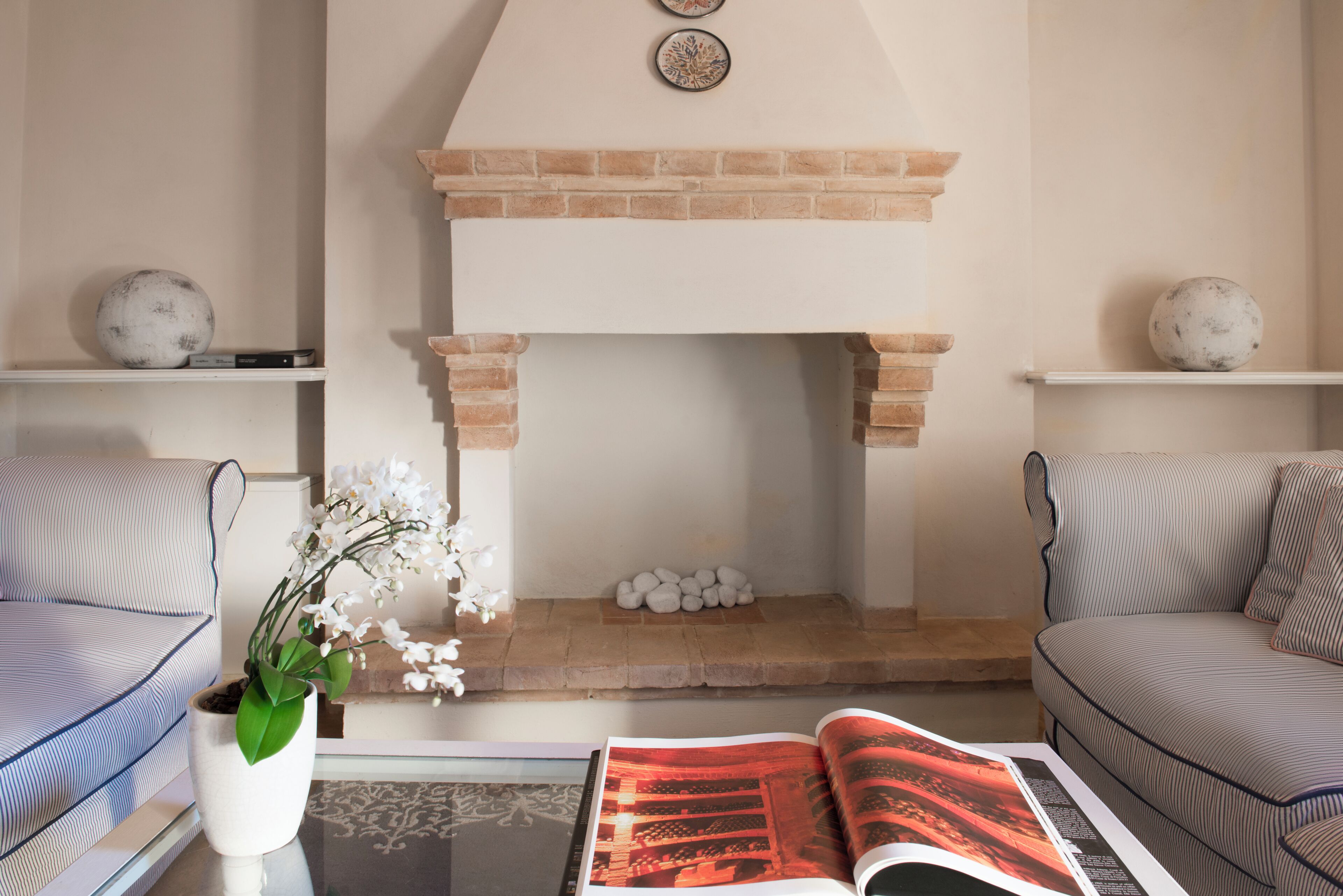 A living room with a fireplace, two sofas, a coffee table with a magazine, and decorative items on shelves.