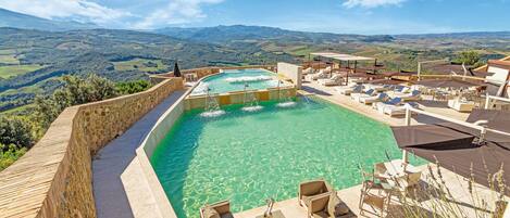 A pool with a view of the countryside, surrounded by lounge chairs and umbrellas.