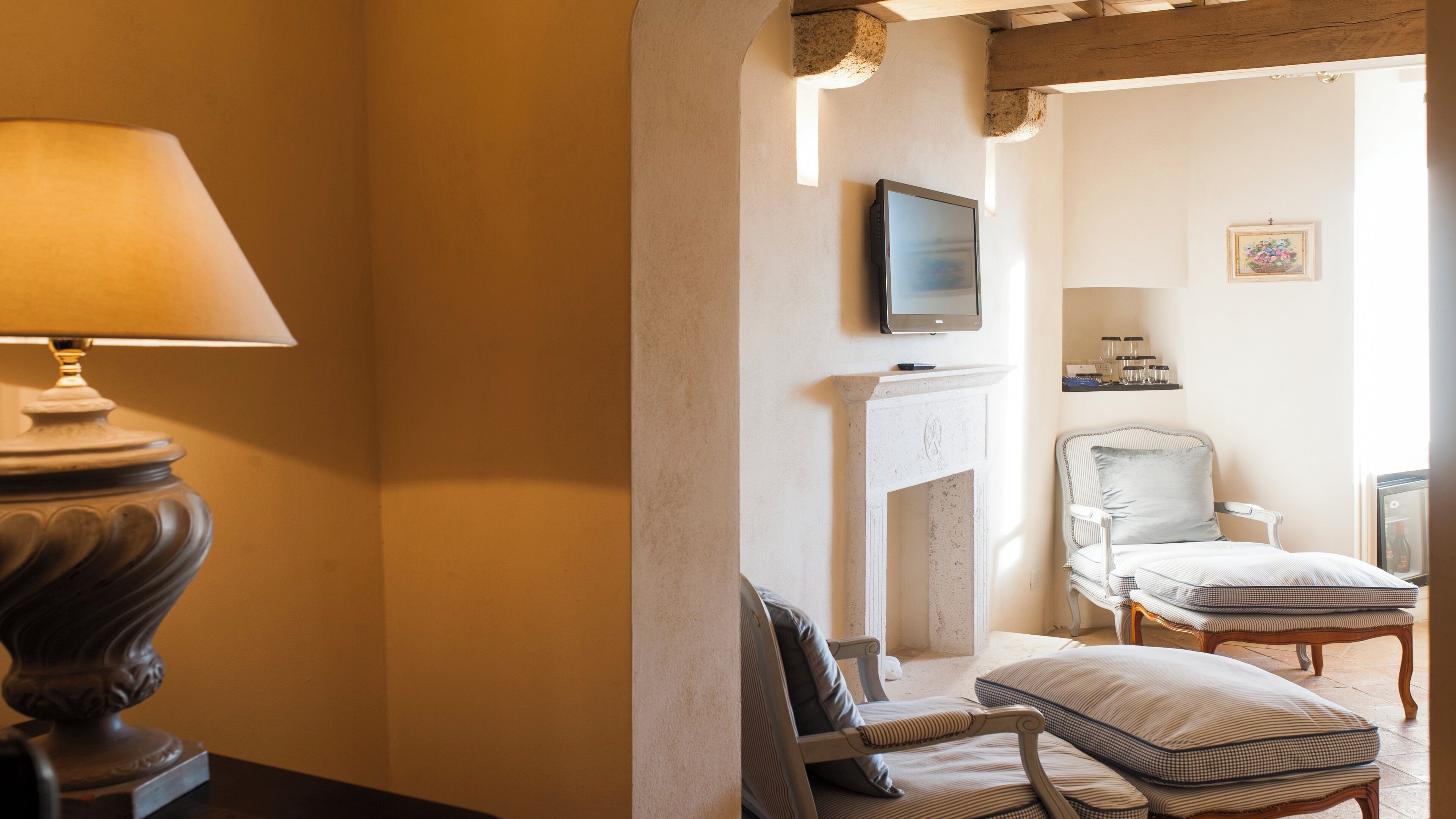 Una habitación con chimenea, un televisor montado encima, una cama con ropa de cama a rayas y un sillón con cojín.
