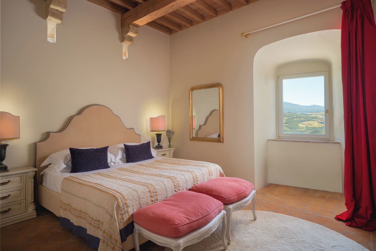A bedroom with a bed, bedside tables, a window with a view, and a red curtain.