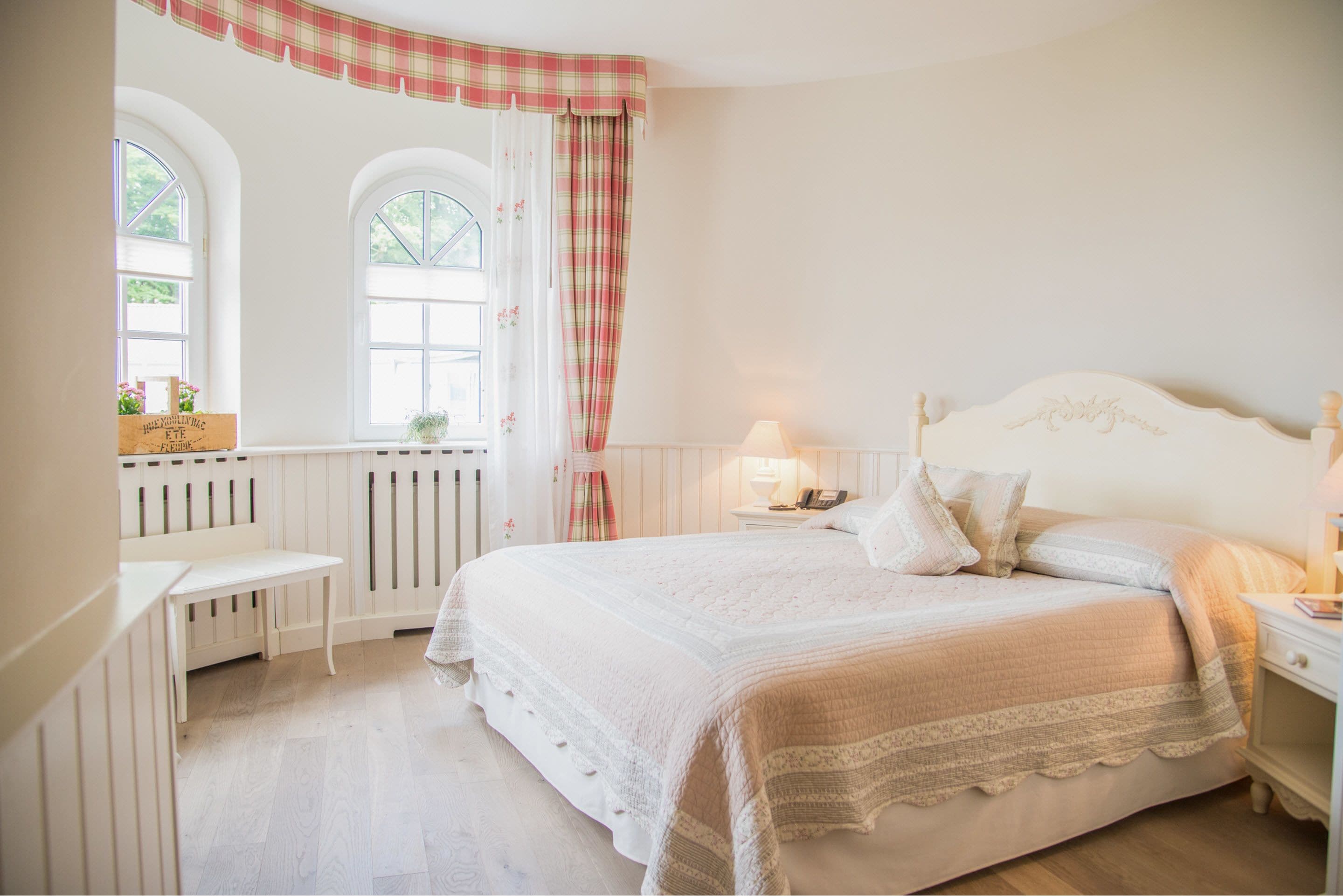 Une chambre à coucher avec un grand lit, une table de chevet, une commode et une fenêtre avec des rideaux.