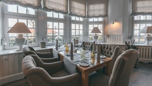 A dining area with a wooden table set for four, large windows with lace valances, and a view of the outside.