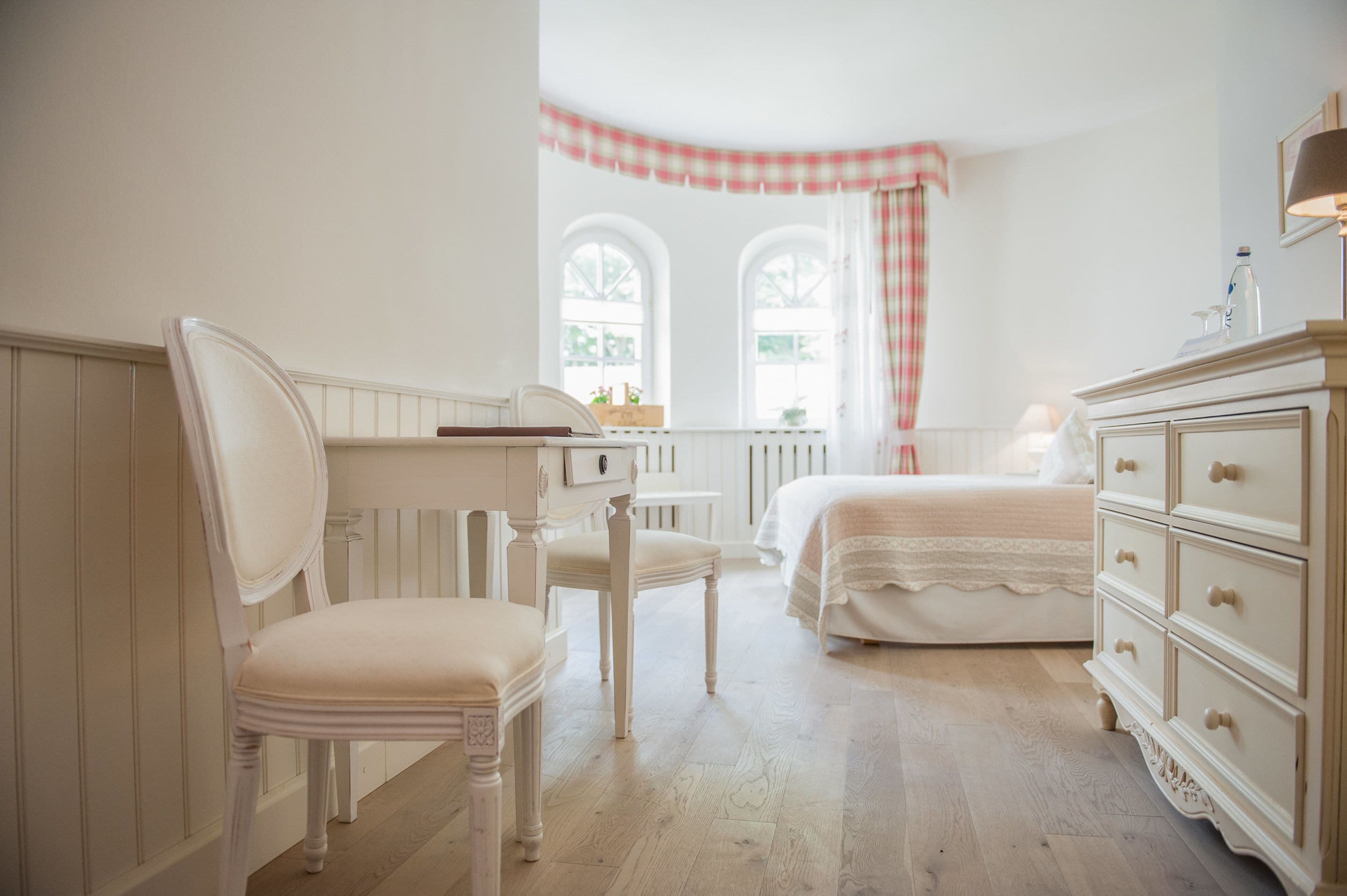 Un dormitorio con cama, cómoda, silla y ventana con cortina a cuadros.