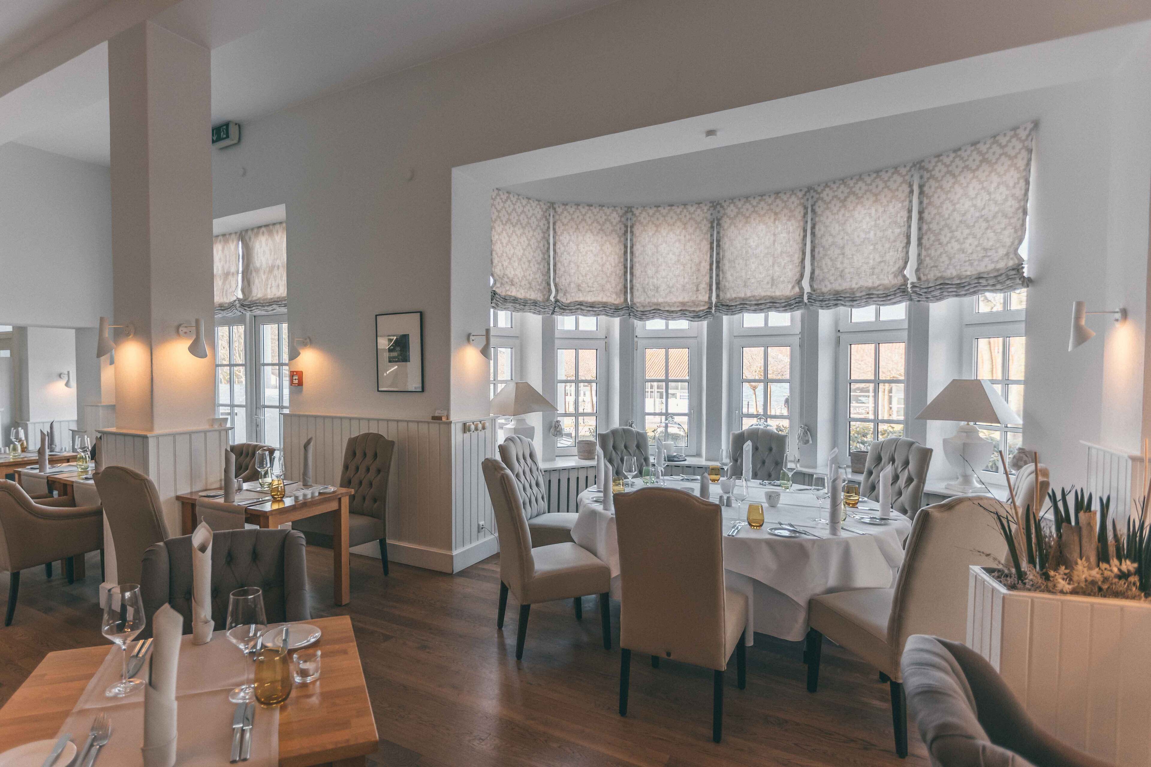 A restaurant with multiple dining tables, chairs, and large windows with patterned curtains.