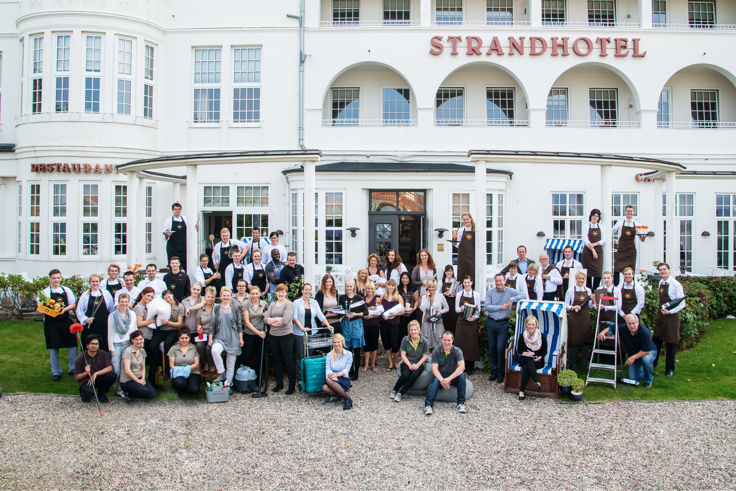 A group of people in front of a building with a sign reading "STRANDHOTEL".