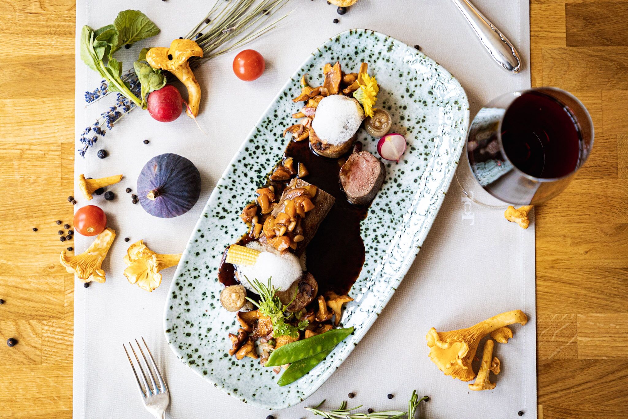 Un plato de comida con diversos vegetales y una copa de vino tinto.