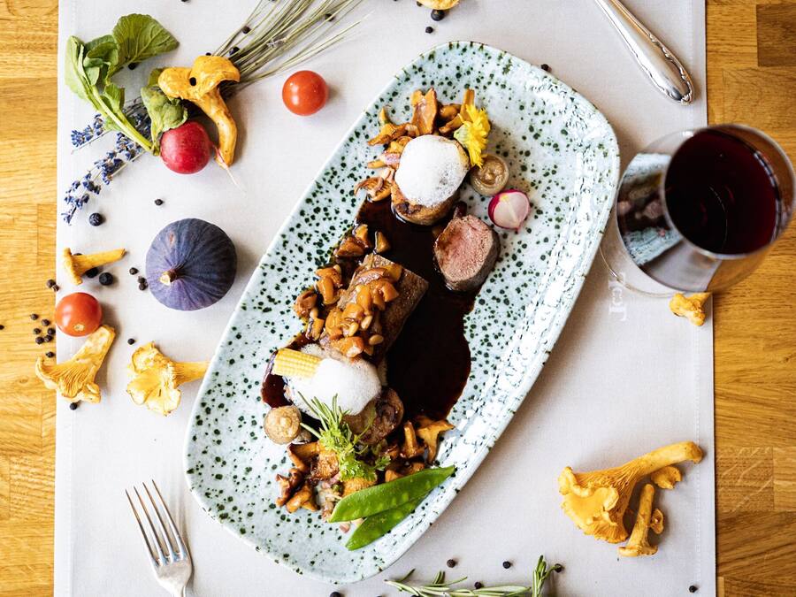 Un plato de comida con diversos vegetales y una copa de vino tinto.