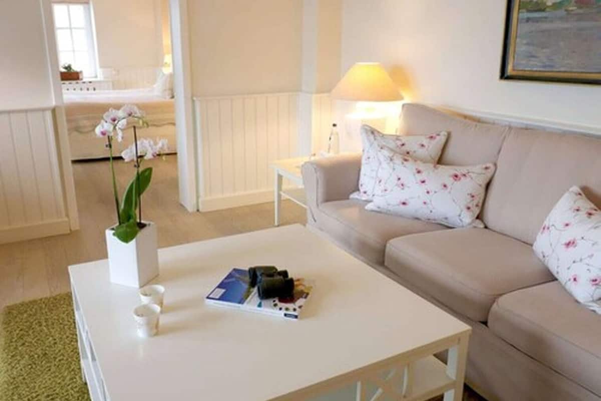 A living room with a beige sofa, a white coffee table, and a vase with flowers.