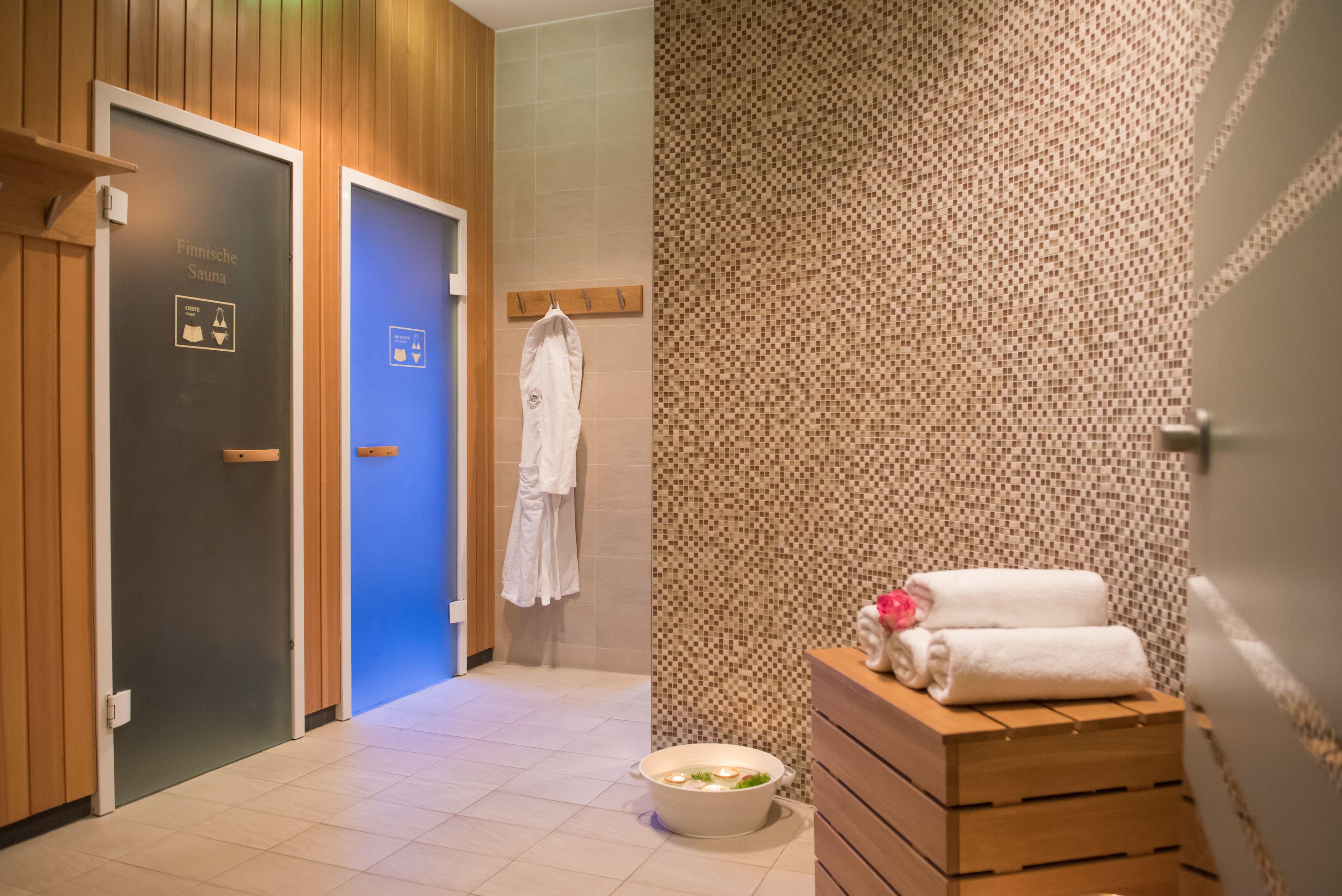 Un vestíbulo de sauna finlandesa con puertas de madera, piso de baldosas y una pared con diseño de mosaico.