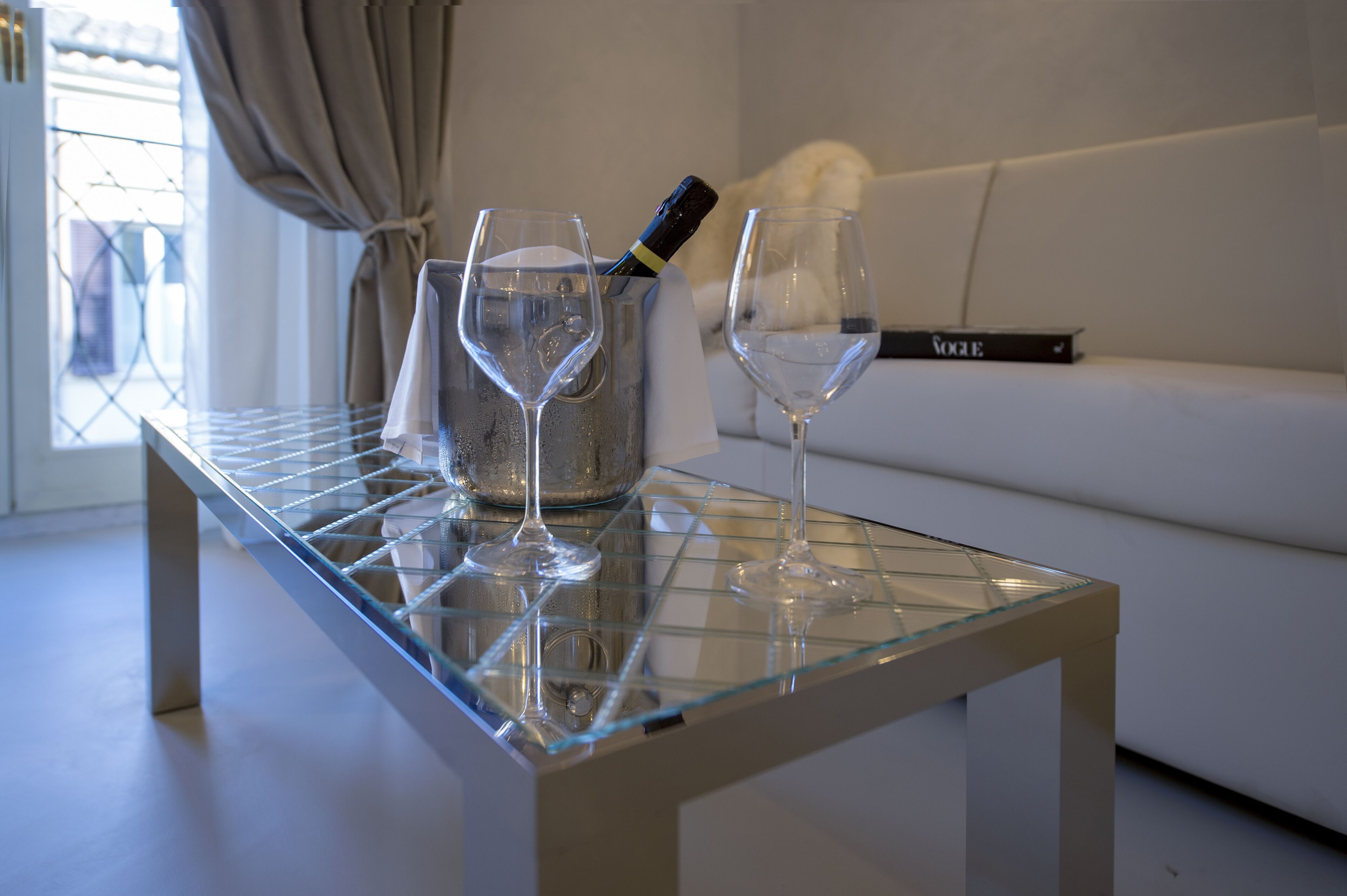 A glass-topped table with two wine glasses and a champagne bottle in a metal container.